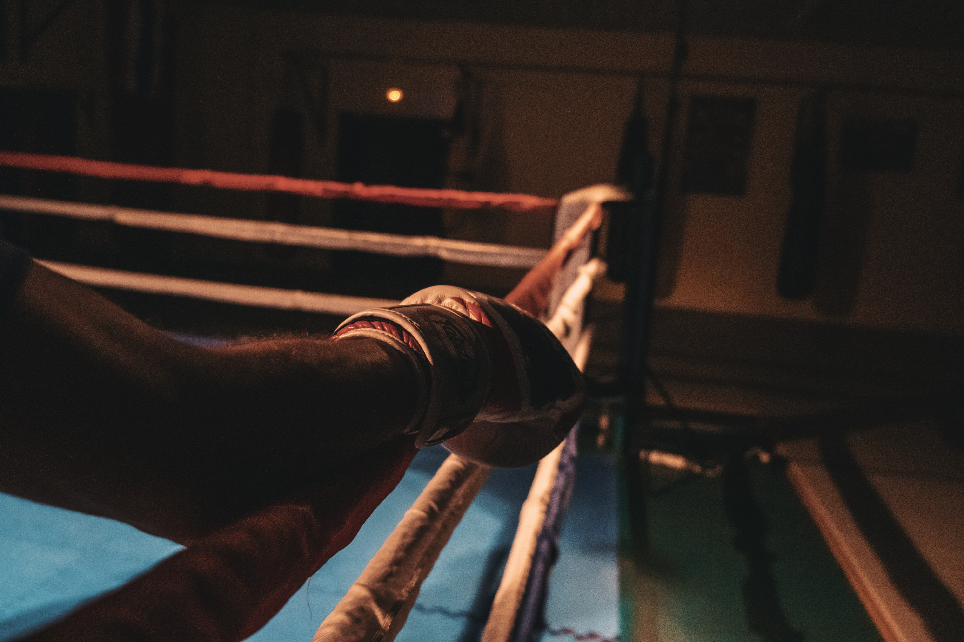 Image of a hand from a person on the side of a boxing ring, leaning on the ropes of the ring